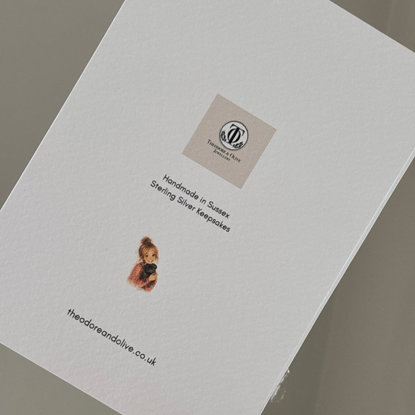 Back of a card showing brand logo and girl with a pug (owner of brand) with website and held by a persons hand
