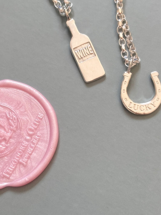 Green background with a theodore and Olive wax seal logo and sterling silver wine bottle and lucky horse shoe charm necklace