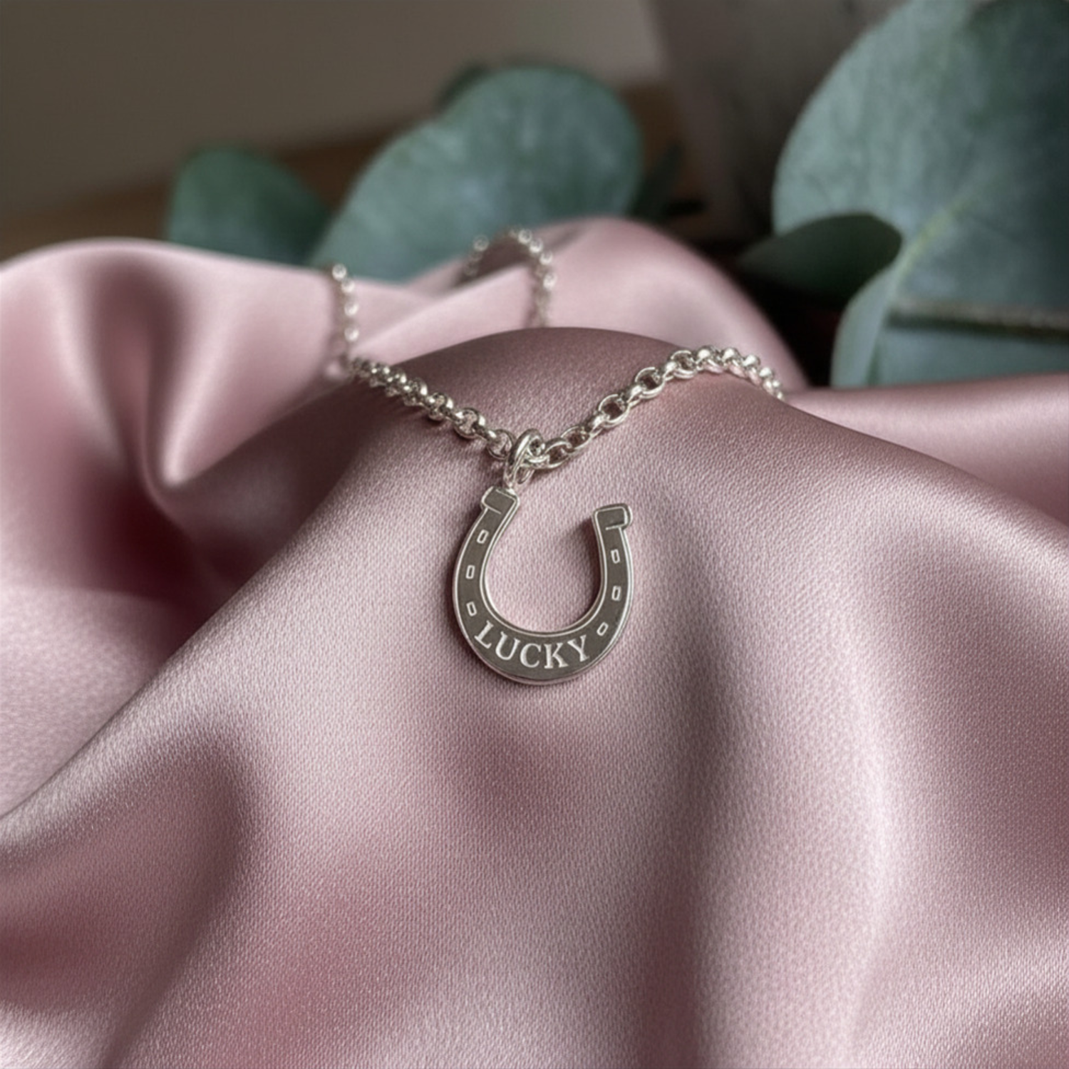 Silver horse shoes charm with lucky engraved on it layed on dusky pink satin