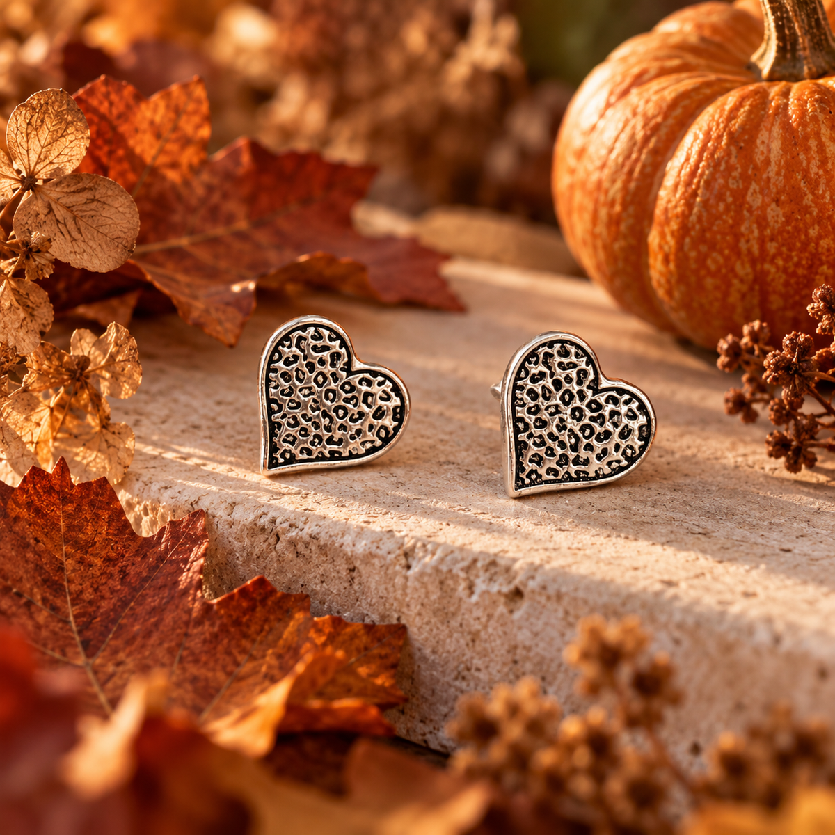 Leopard print heart stud earring surround by autumnal leaves and pumpkins 