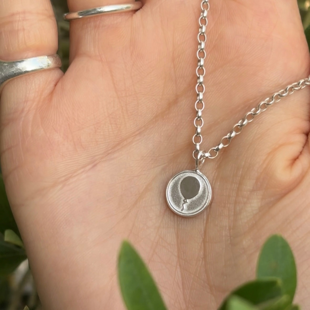 Silver necklace with a round pendant on a hand against a natural background