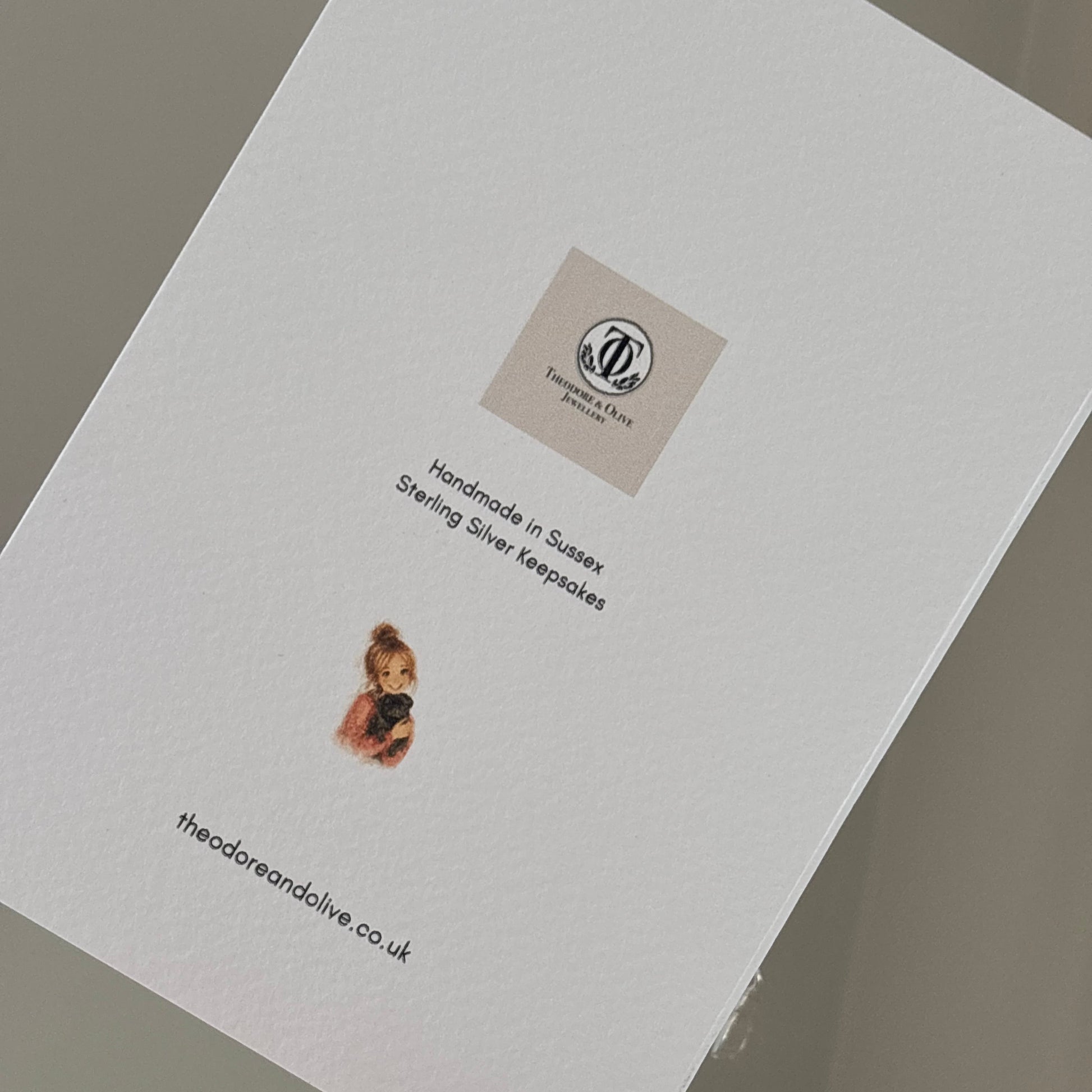 Back of a card showing brand logo and girl with a pug (owner of brand) with website and held by a persons hand