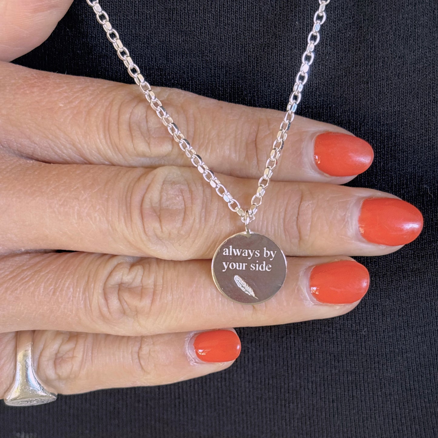Silver necklace with a pendant on a hand with orange nail polish against a black background