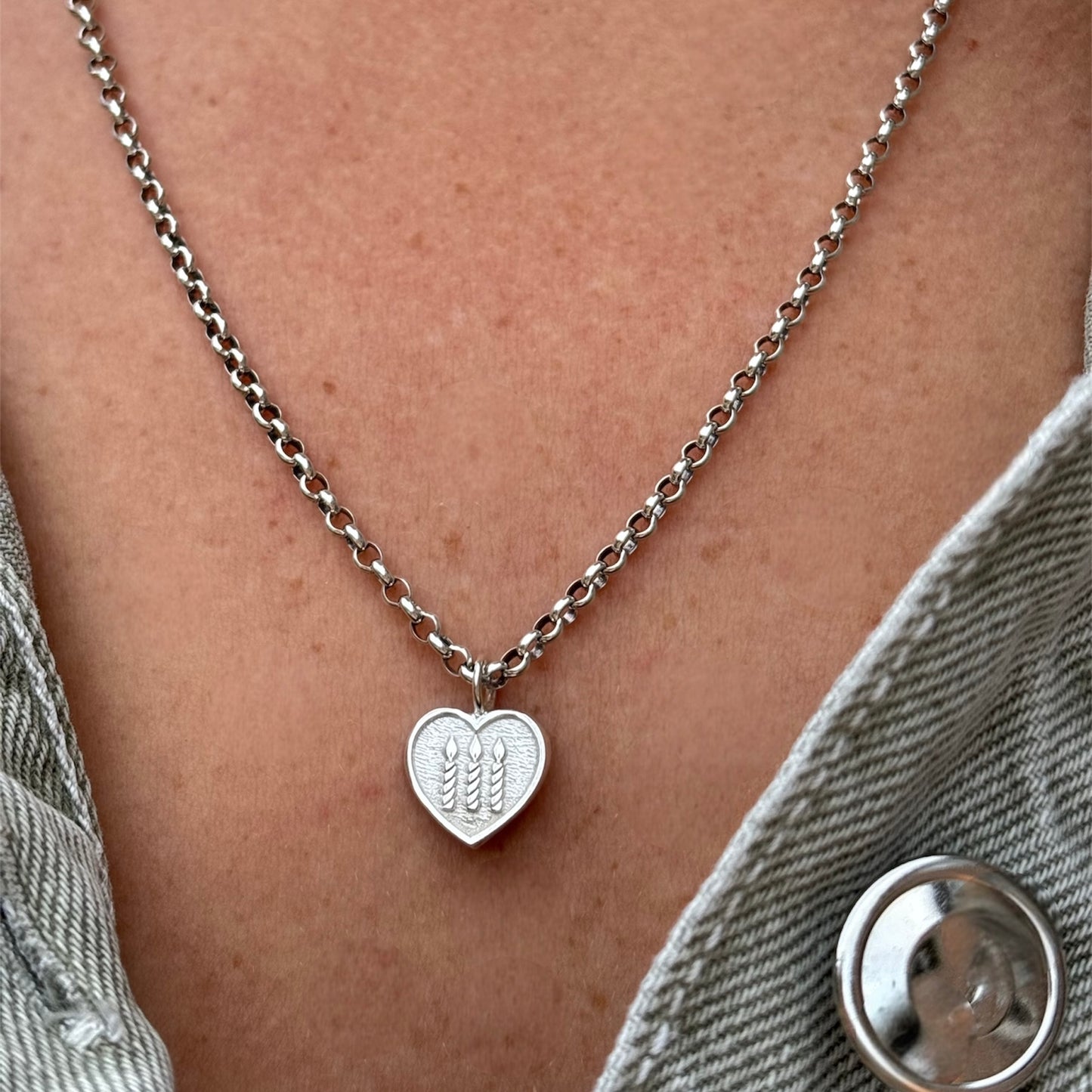 Silver necklace with heart shape pendant with three candles engraved on the front worn by a person
