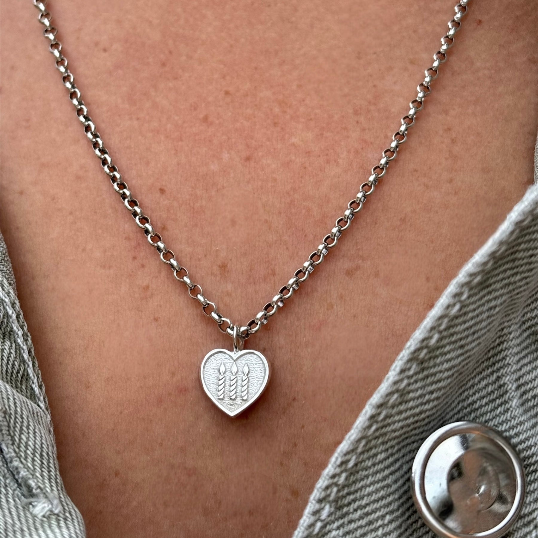 Silver necklace with heart shape pendant with three candles engraved on the front worn by a person