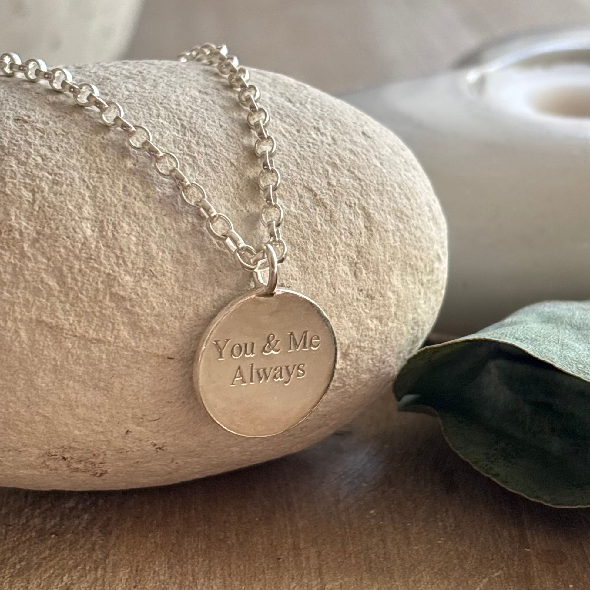 Sterling silver disc necklace engraved with the words “You & Me Always” on a fine silver chain, stone surface