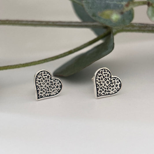 Sterling silver leopard print heart stud earrings on a white background with eucalyptus leaves