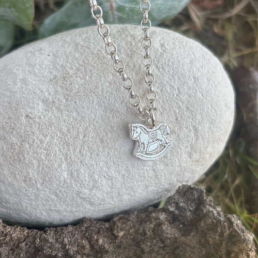 Silver belcher chain with a silver rocking horse pendant with a outdoor background 