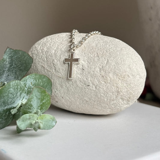 Silver cross necklace on a white stone with greenery