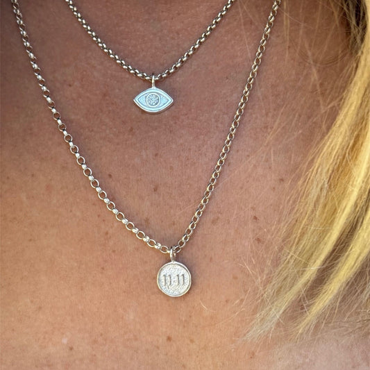 Close-up of layered necklaces with eye and '1111' pendant on a person's neck.