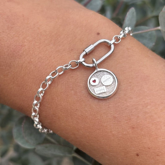 Silver bracelet with a round charm on a wrist against a natural background
