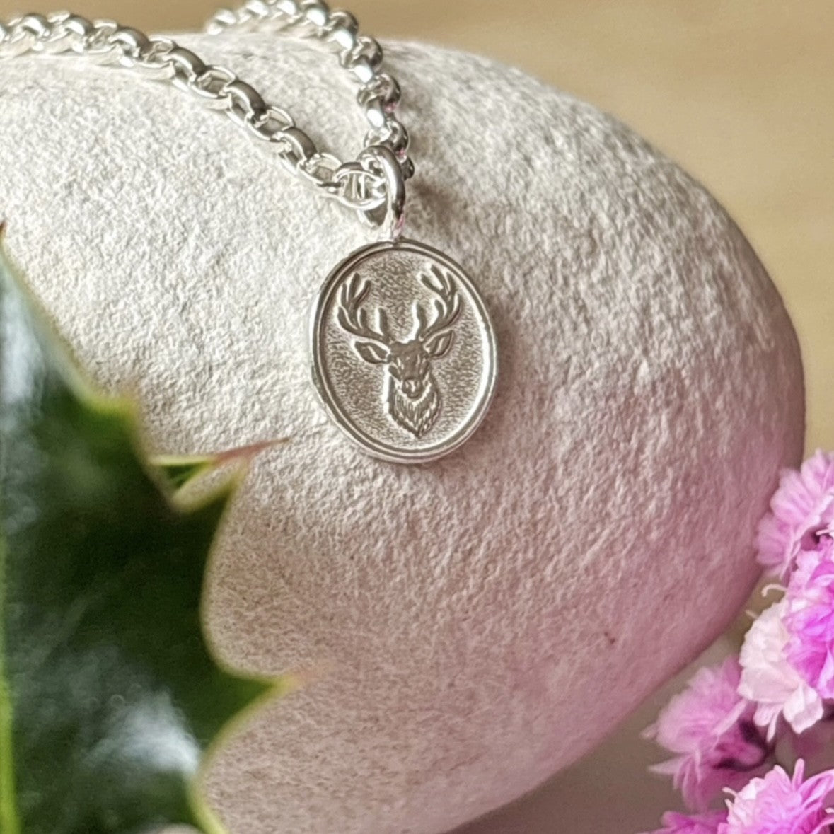 Silver necklace with a deer pendant on a textured white surface with pink flowers.