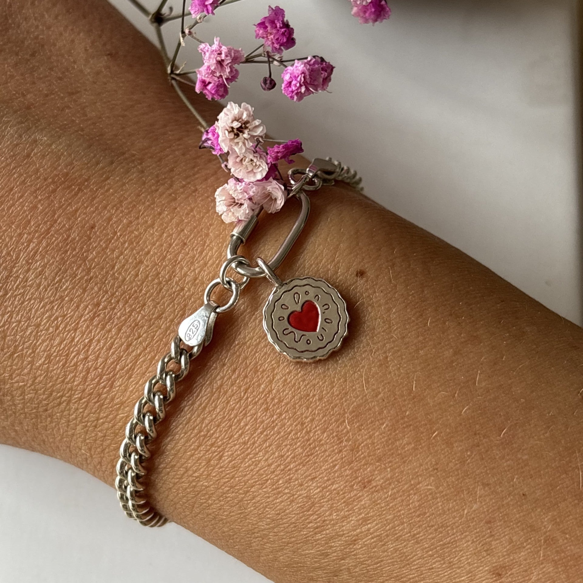 Curb chain Bracelet with heart jammy dodger charm on wrist, surrounded by pink flowers