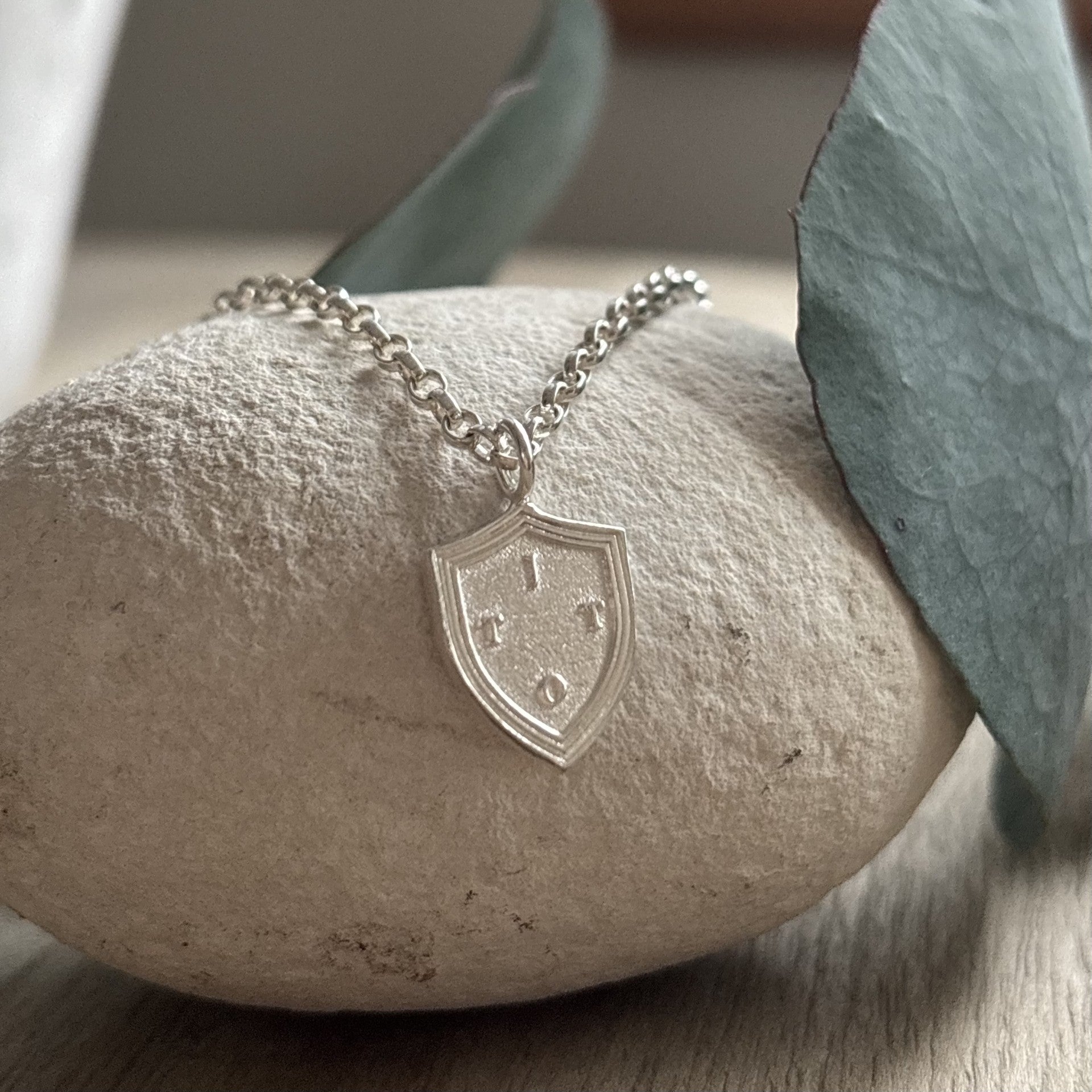Personalised sterling silver family shield initial pendant necklace, layer on a white stone with free surrounding eucalyptus 