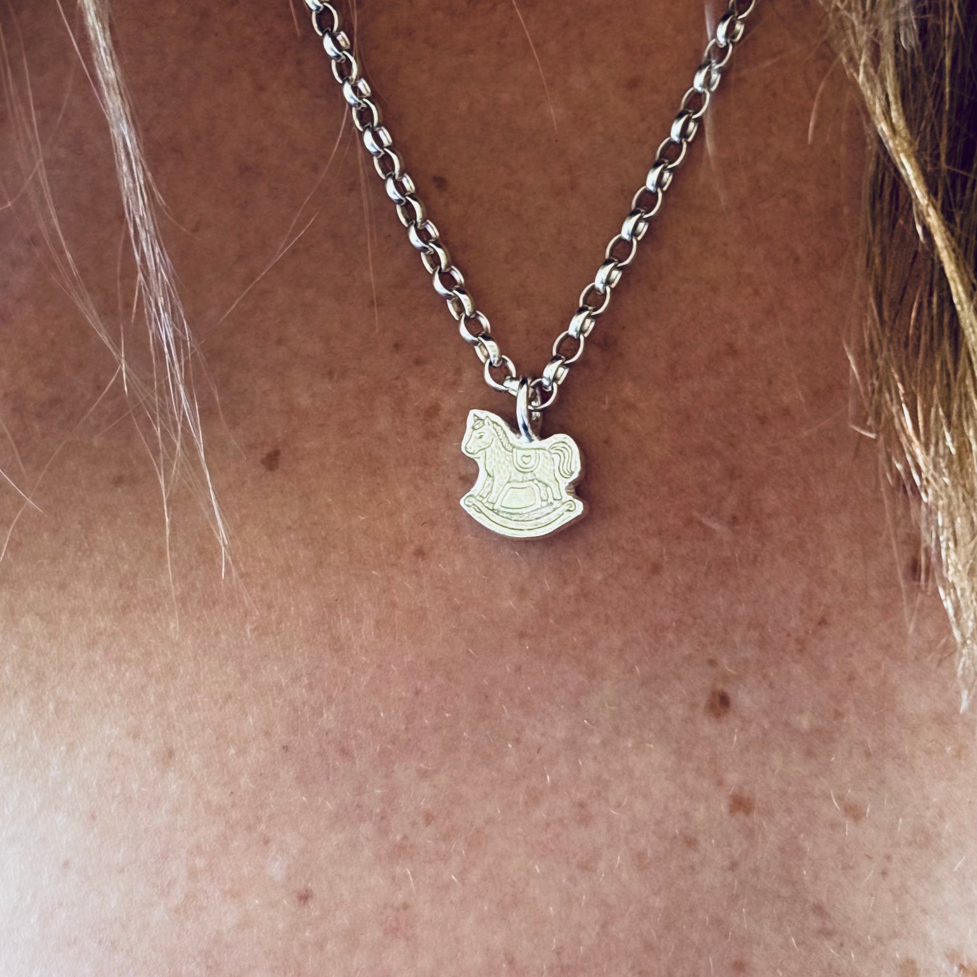 Silver necklace with a rocking horse pendant on a person's neck.