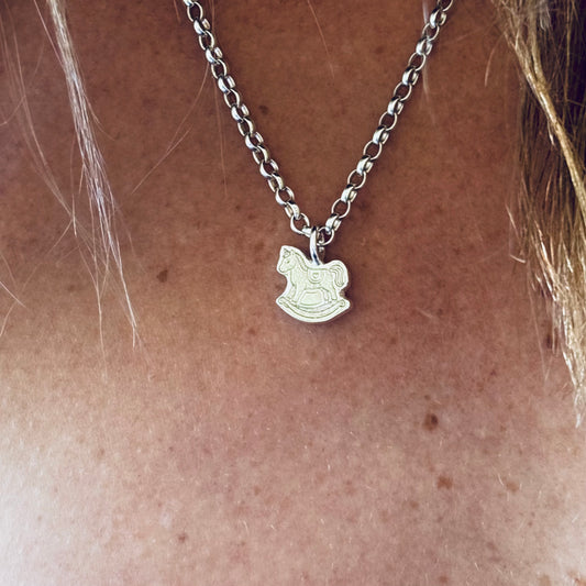 Silver necklace with a rocking horse pendant on a person's neck.