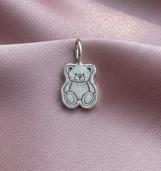Silver teddy bear charm on a pink satin background