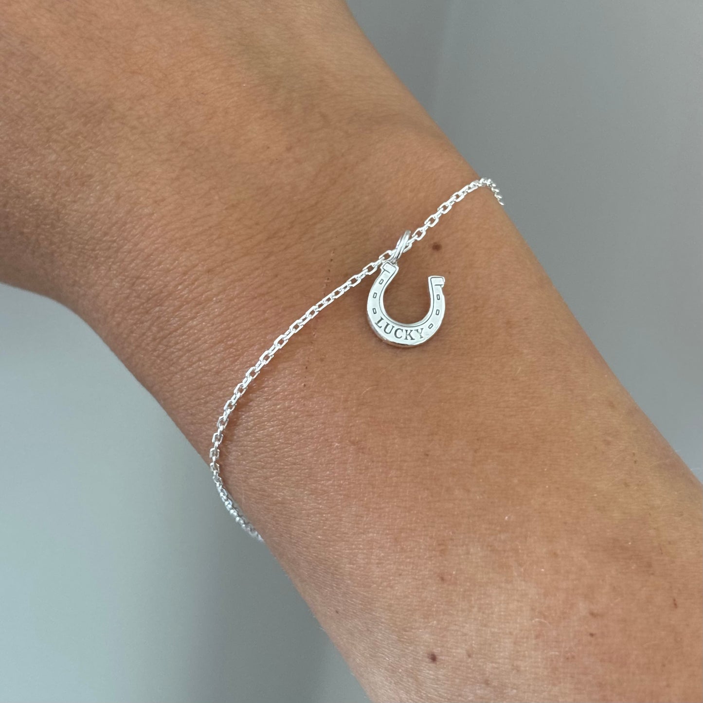 Dainty Sterling silver bracelet with a lucky horse shoes charm placed on a wrist