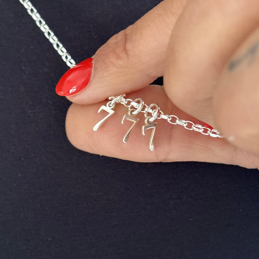 Silver necklace with a number '7' pendant held by a hand against a dark background