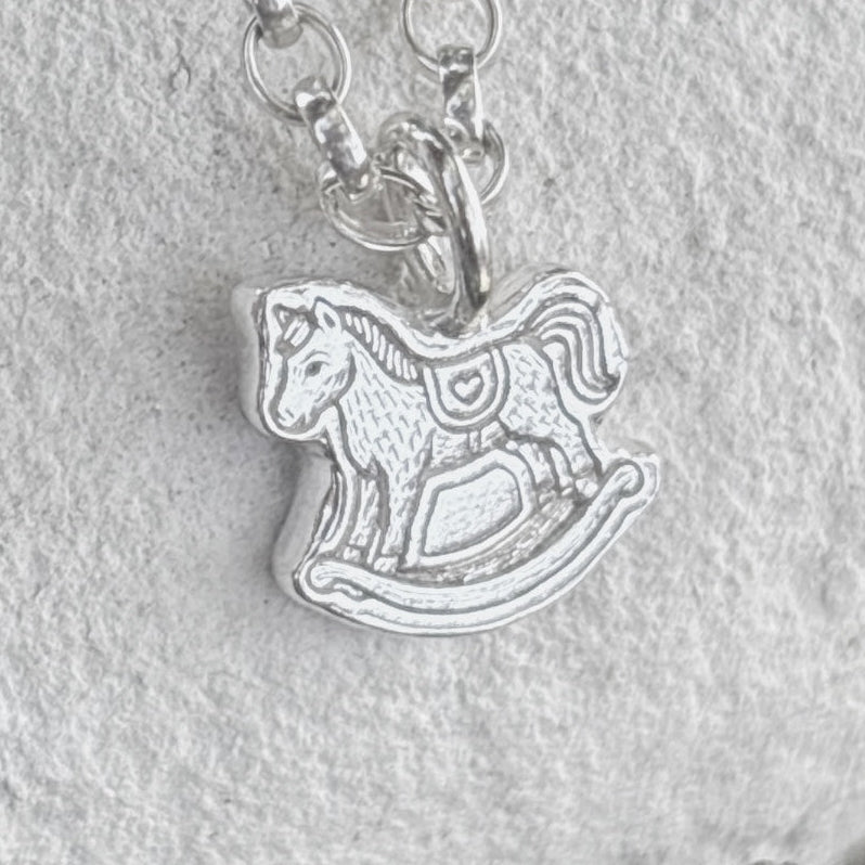 Silver rocking horse pendant on a chain against a light gray background