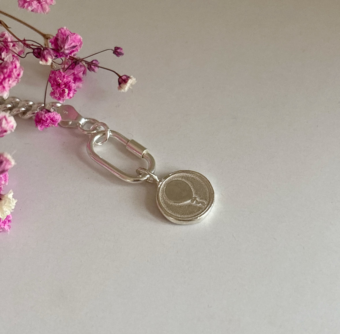 Handmade sterling silver balloon charm photographed on a curb chain with pink gypsophila flowers, symbolising joy, celebration and meaningful moments