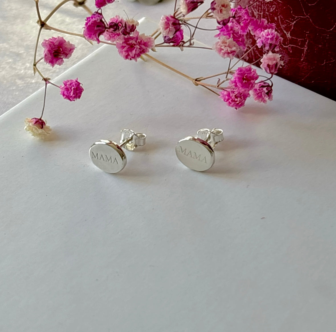 Sterling silver MAMA stud earrings displayed beside pink dried flowers on a white background
