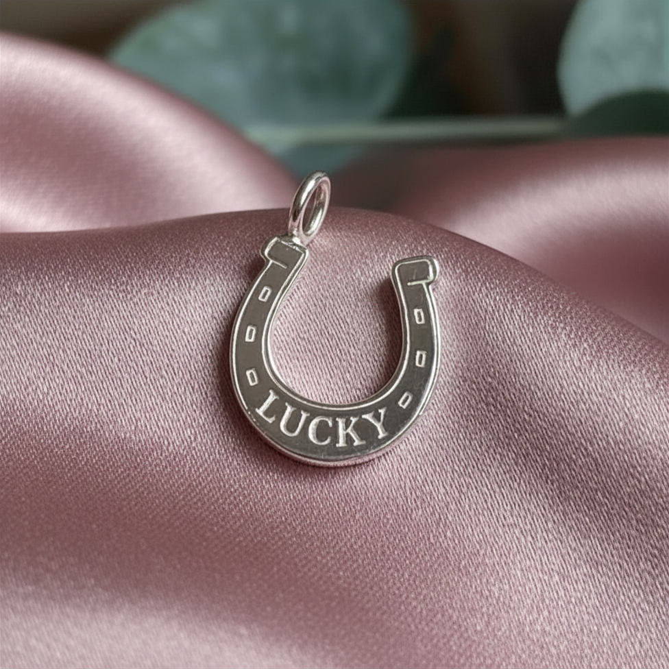 Silver horseshoe-shaped pendant with 'LUCKY' engraving on pink satin fabric