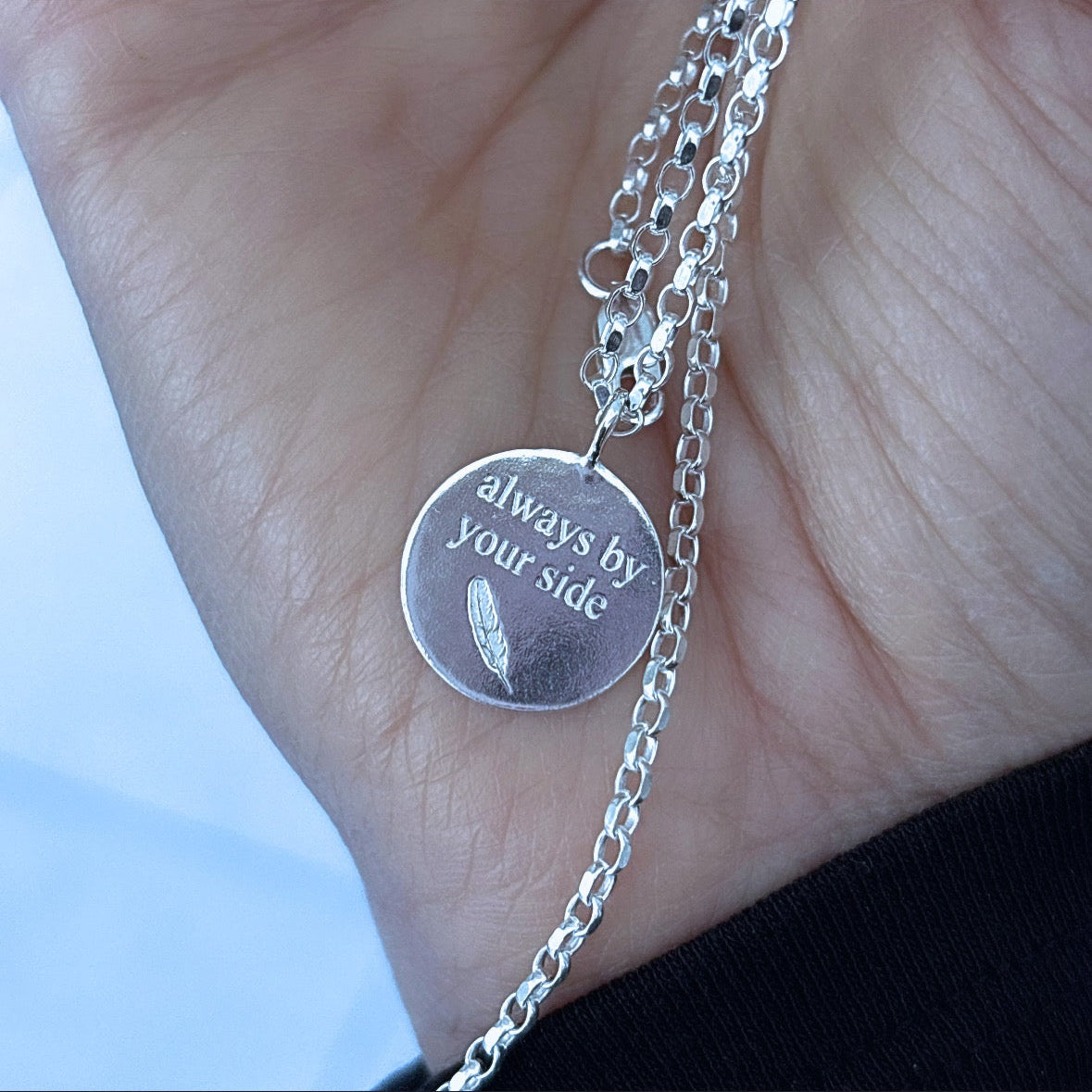 Silver necklace with a pendant on a hand against a neutral background
