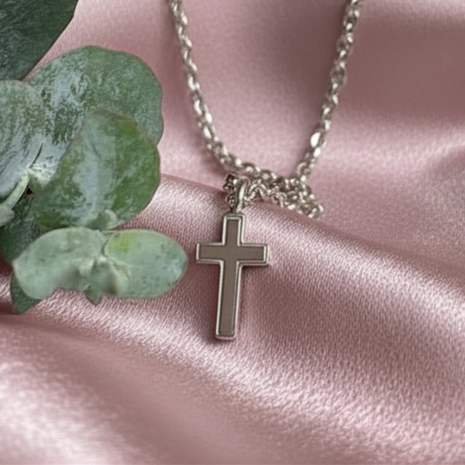 Silver necklace with a cross pendant on pink fabric with green leaves.