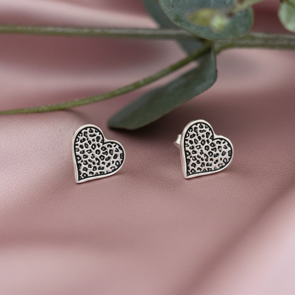 Heart-shaped earrings with a leopard print pattern on a pink surface with green leaves.