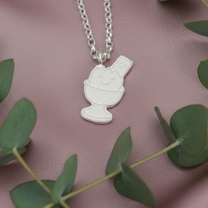 Silver necklace with a pendant on a pink fabric background with green leaves