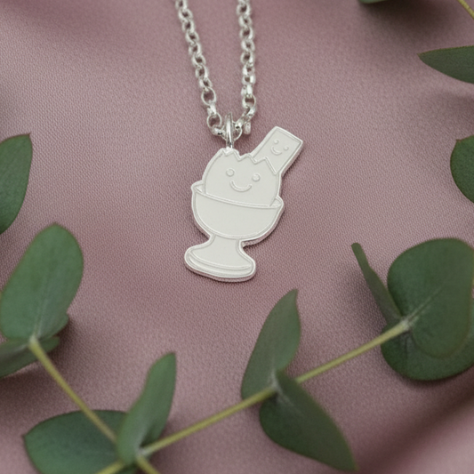 Silver necklace with a pendant on a pink fabric background with green leaves