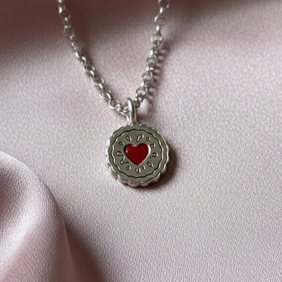 Silver necklace with a jammy Dodger heart pendant on a pink fabric background