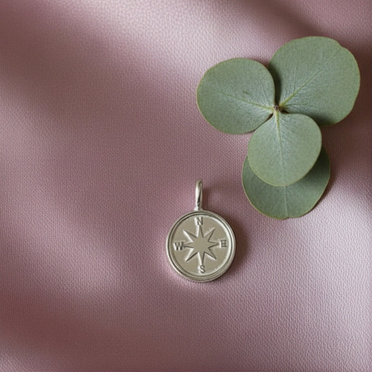 Silver charm with compass design on a pink fabric background