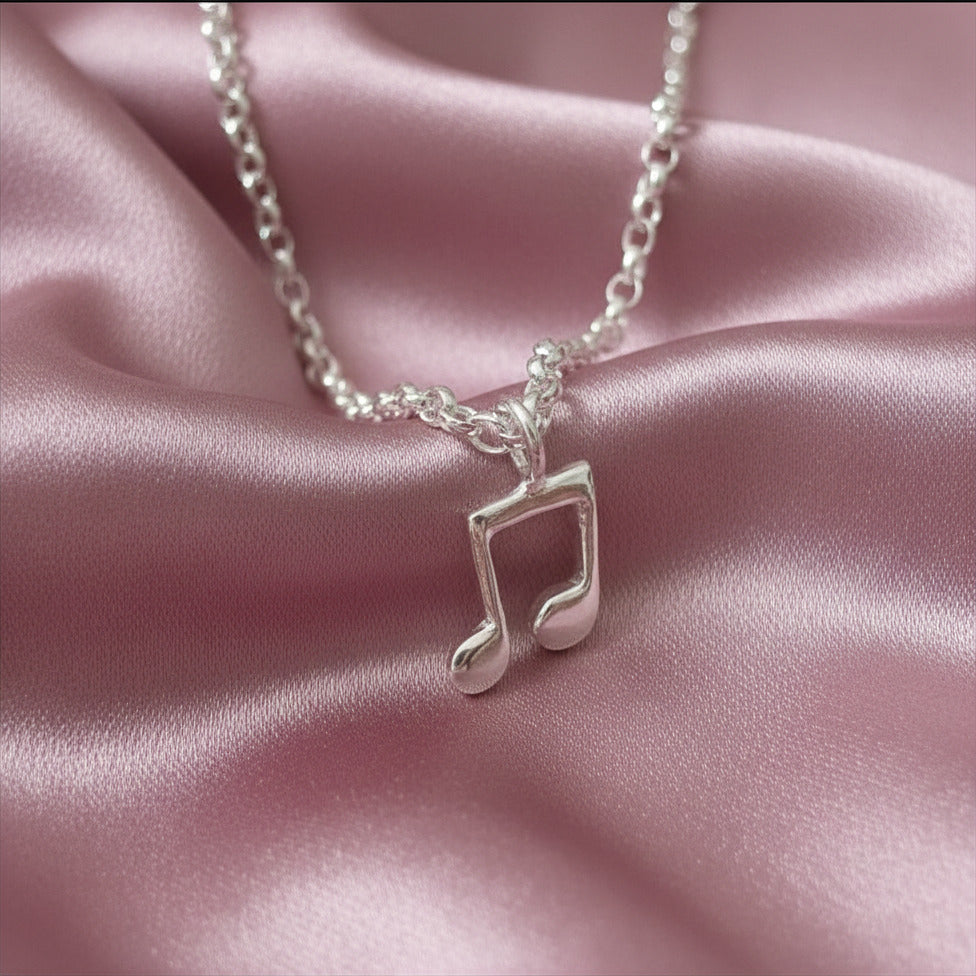 Silver necklace with a music note pendant on a pink satin background