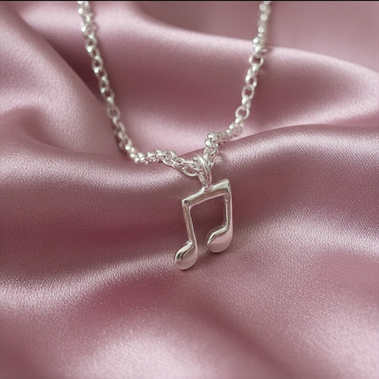 Silver necklace with a music note pendant on a pink satin background
