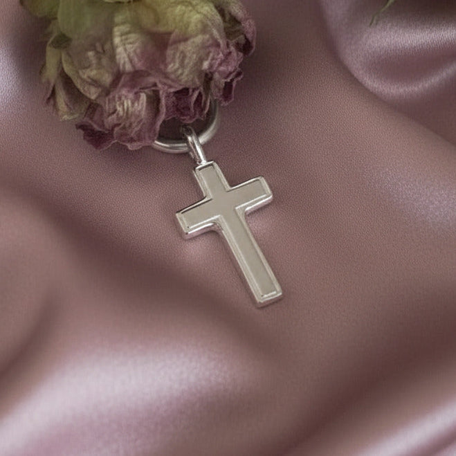 Silver cross pendant on a dried flower arrangement against a pink fabric background