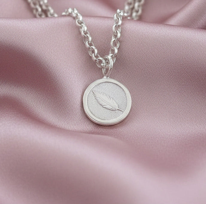 Silver necklace with a round pendant on a pink fabric background
