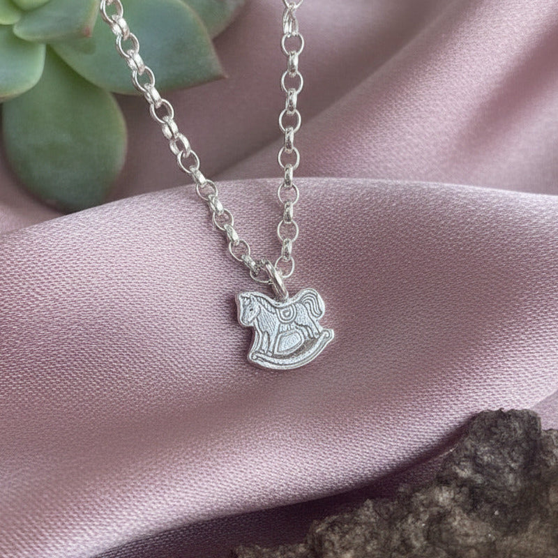 Silver necklace with a pendant on pink fabric with a succulent in the background