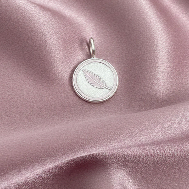 Silver pendant with feather design on a pink satin background