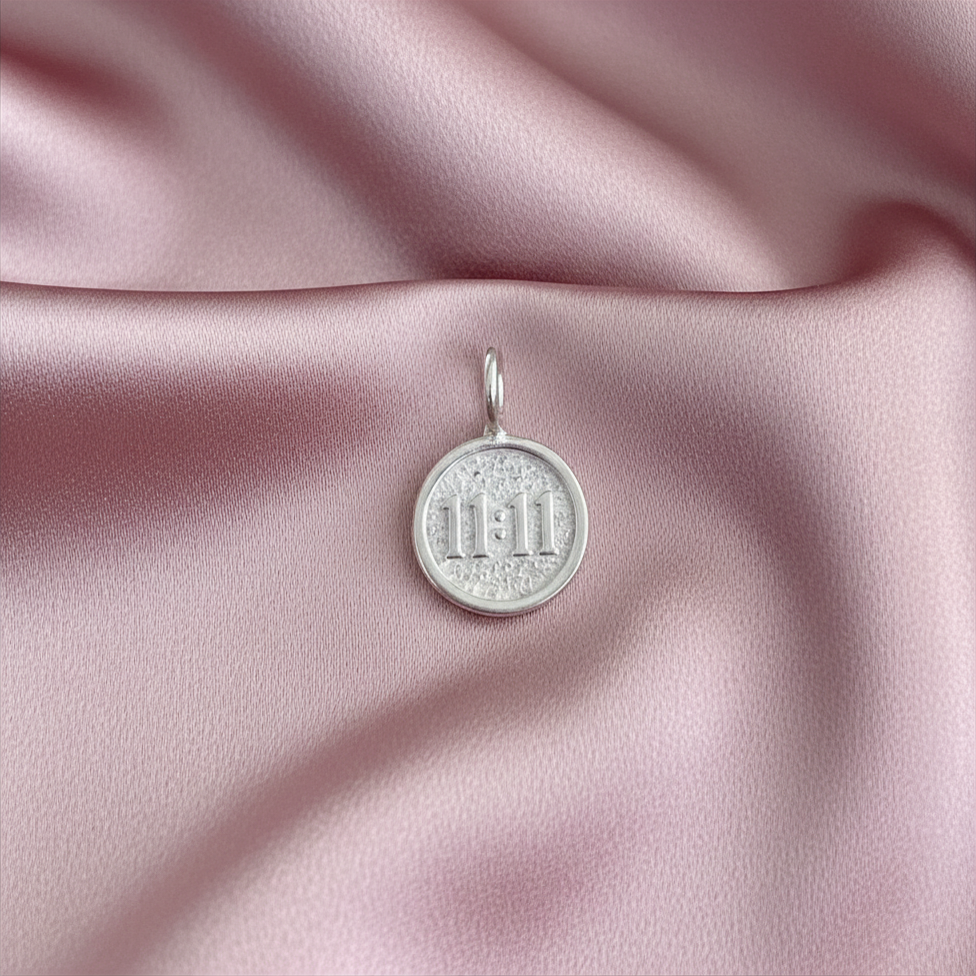 Silver pendant with '11:11' engraving on pink satin fabric