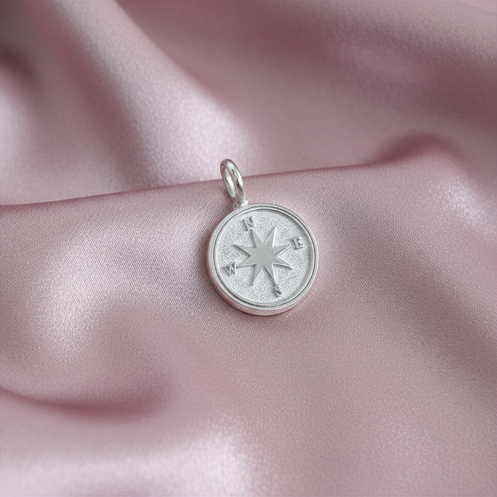 Silver compass pendant on a pink satin background