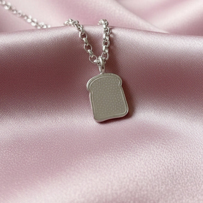 Silver necklace with a toast pendant on a pink satin background