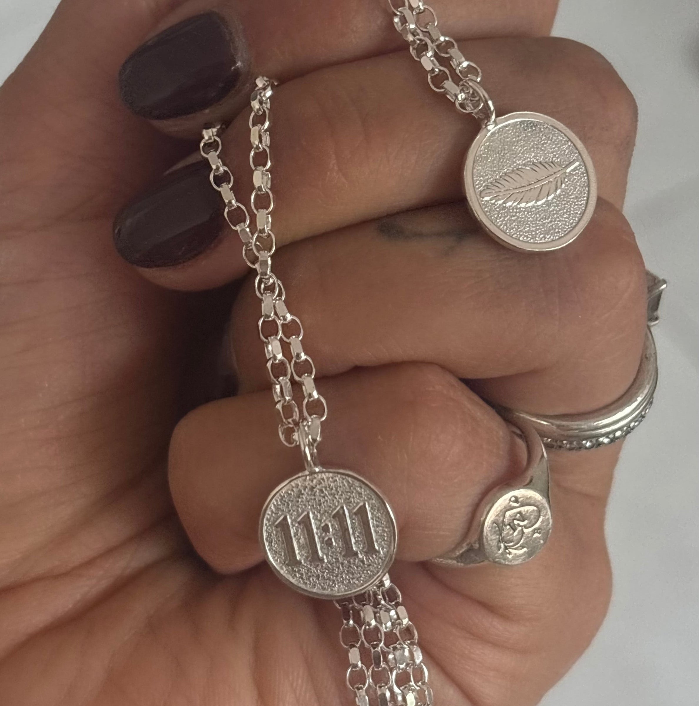 Hand holding two silver necklaces. One necklace with 11:11 in 3d engraving and the second a 3d engraved feather. 