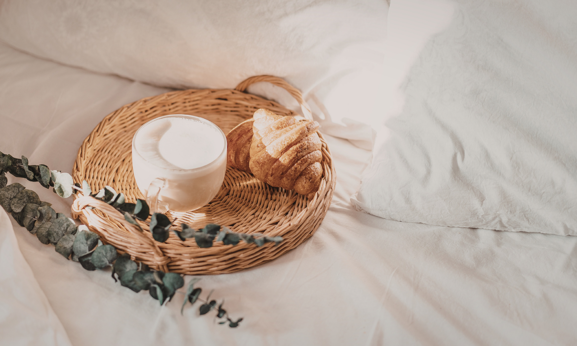 Wicker basket with a white cup and croissant on a light surface