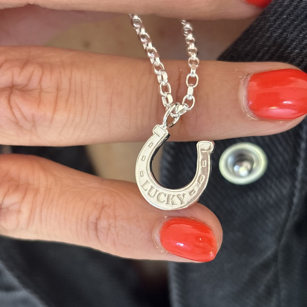 Silver lucky horse shoe pendant held by a hand with link nails 